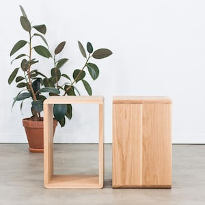 May include: Two wooden stools, one with an open frame and the other with a solid front. Both stools are made of light-coloured wood and have a simple, modern design.