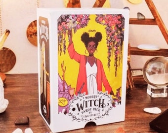 May include: White box with a colorful illustration of a woman with dark skin holding a wand. The box says "Modern Witch Tarot Deck by Lisa Sterle".