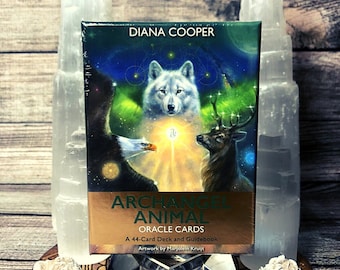 Può includere: Un mazzo di 44 carte oracle intitolato "Archangel Animal Oracle Cards" con un libro guida. La scatola presenta un'illustrazione colorata di un lupo, un'aquila e un cervo su uno sfondo dorato. Illustrazione di Marjolein Kruijt.