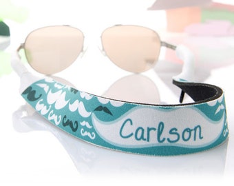 May include: White and teal blue eyeglass strap with a mustache pattern and the name "Carlson" printed on it.