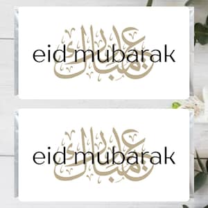 May include: Two white cards with the text "eid mubarak" in black lettering and a gold Arabic calligraphy design.