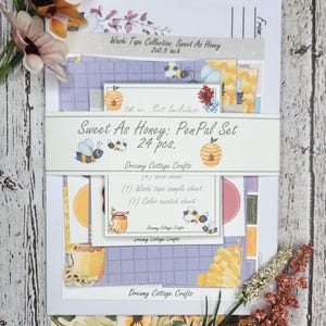 May include: A set of 24 bee-themed washi tape sheets and a sample sheet. The set is called "Sweet As Honey: PenPal Set" and is made by Dreamy Cottage Crafts. The sheets are purple, yellow, and white with bees, honeycombs, and jars of honey.