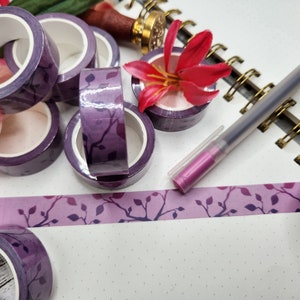 May include: Purple washi tape rolls with a leaf pattern, a pink flower, a pen, and a notebook with gold rings.