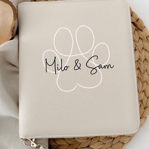 Könnte beinhalten: Eine beige Reißverschlusstasche mit einem weißen Pfotenabdruck-Design und dem Text "Milo & Sam" in Schwarz.