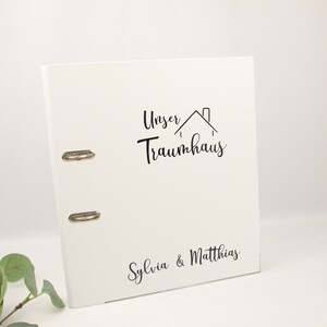 Könnte beinhalten: Weißer Ordner mit schwarzer Aufschrift "Unser Traumhaus" und "Sylvia & Matthias".