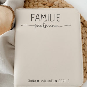 Könnte beinhalten: Ein cremefarbener Lederordner mit dem Text "FAMILIE paulmann" und "JANA ♥ MICHAEL ♥ SOPHIE" darauf gedruckt. Der Ordner hat einen Reißverschluss und einen weißen Riemen.