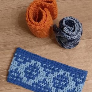 May include: Two crocheted headbands, one orange and one blue with a geometric pattern. The blue headband is lying flat on a wooden surface.
