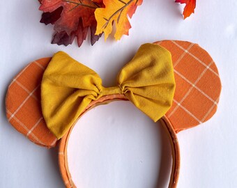 May include: Orange and white plaid fabric mouse ears with a yellow bow. The headband is brown.