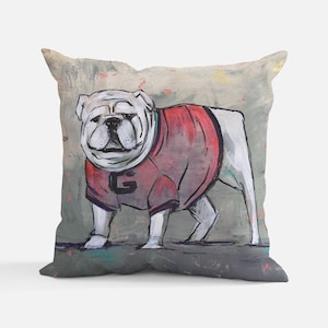 May include: A white bulldog wearing a red jersey with a white 'G' on the front. The bulldog is standing on a gray and green background.