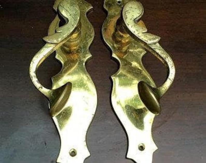 K&ouml;nnte beinhalten: Ein Paar antike Messing-T&uuml;rgriffe mit verzierten, dekorativen Designs. Die Griffe haben eine einzigartige, geschwungene Form und eine glatte, polierte Oberfl&auml;che.