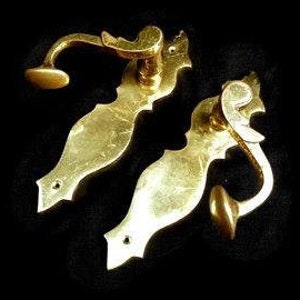 K&ouml;nnte beinhalten: Zwei verzierte Messing-T&uuml;rgriffe mit einem dekorativen Design. Die Griffe haben eine gebogene Form und einen kleinen Knopf am Ende.