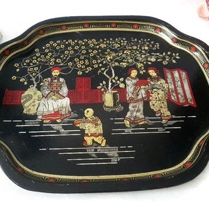 May include: Black metal serving tray with a gold and red design featuring a scene of people in traditional Chinese clothing standing under a flowering tree.