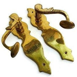 Könnte beinhalten: Zwei verzierte Messing-Türgriffe mit einem dekorativen Design. Die Griffe haben eine gebogene Form und einen kleinen Knopf am Ende.