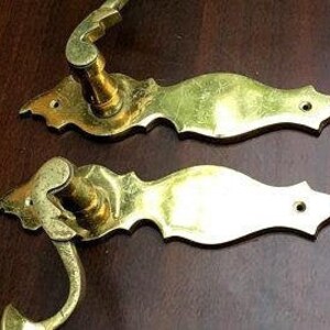K&ouml;nnte beinhalten: Zwei antike Messing-T&uuml;rgriffe mit verzierten Designs. Die Griffe haben einen Hebelmechanismus und eine dekorative R&uuml;ckplatte.