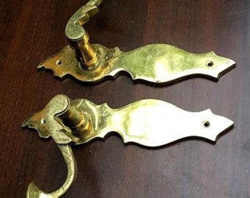 K&ouml;nnte beinhalten: Zwei antike Messing-T&uuml;rgriffe mit verzierten Designs. Die Griffe haben einen Hebelmechanismus und eine dekorative R&uuml;ckplatte.