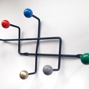 Pode incluir: Um cabide de metal preto com seis ganchos. Os ganchos são rematados com bolas coloridas em azul, vermelho, verde, dourado e cinza.