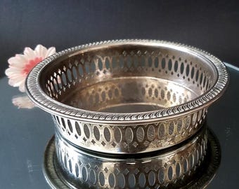 May include: Silver-plated coaster with a decorative, openwork design. The coaster has a raised, beaded edge and a circular shape.
