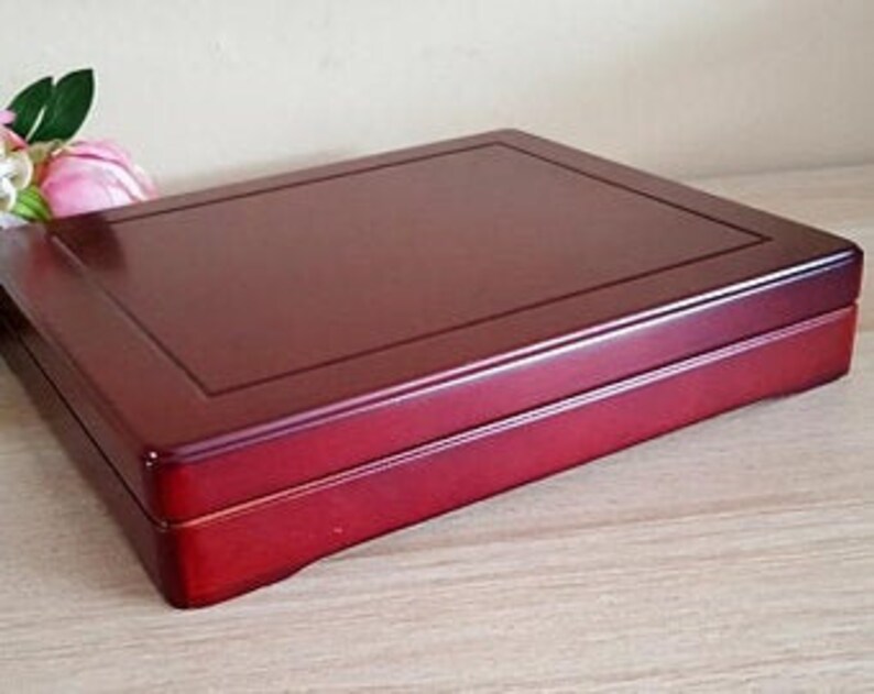 May include: A rectangular, lacquered wooden box in a deep red hue. The box features a slightly raised, rectangular border on the lid and a clean, minimalist design. The box is likely used for storage or display of small items.