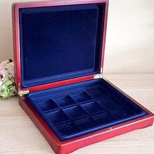 May include: Open wooden jewelry box with a red exterior and a deep blue velvet interior. The box is rectangular with a hinged lid and a tray divided into compartments. The box is empty and sits on a light-colored surface.