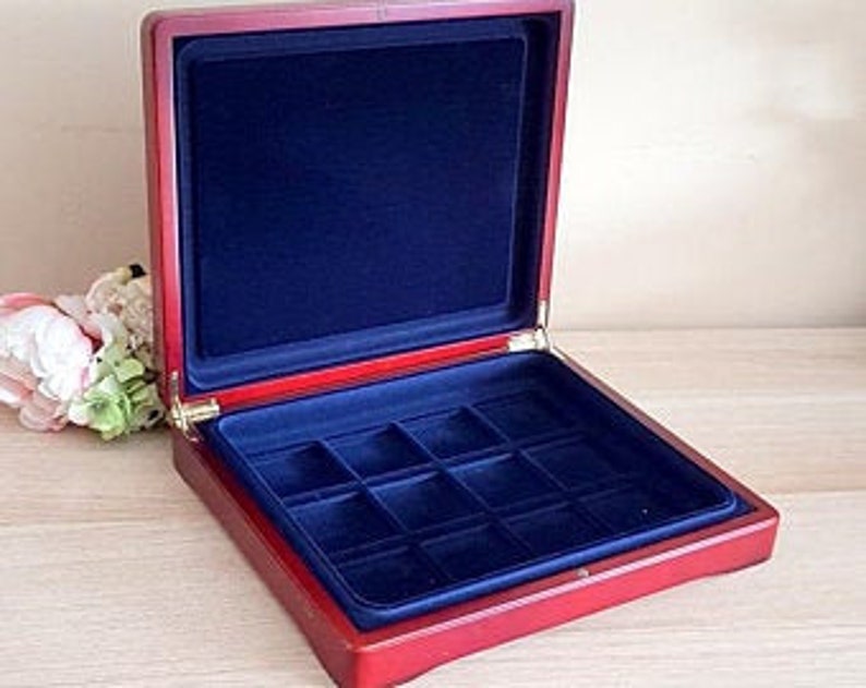 May include: Open wooden jewelry box with a red exterior and a deep blue velvet interior. The box is rectangular with a hinged lid and a tray divided into compartments. The box is empty and sits on a light-colored surface.
