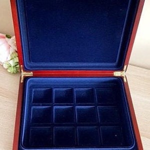 May include: Open wooden jewelry box with a red exterior and a deep blue velvet interior. The box has a rectangular shape with a hinged lid and gold-colored hardware. The interior features a grid of square compartments.
