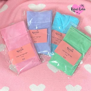 May include: Four pairs of colorful thigh-high stockings in pink, lavender, turquoise, and green, each packaged in clear plastic. Each package has a pink label with the text "Rebel Cute" and "Super Soft Thigh Highs S-XL".