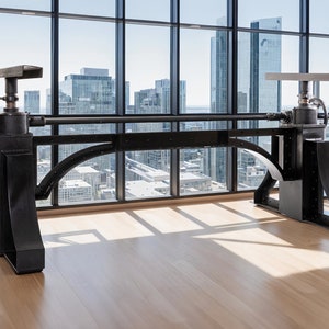 Könnte beinhalten: Ein schwarzer Metallschreibtisch mit einem einzigartigen industriellen Design, ausgestattet mit einem großen Getriebemechanismus und einem langen, horizontalen Balken. Der Schreibtisch befindet sich in einem modernen Büro mit einem großen Fenster, das einen Blick auf die Skyline der Stadt bietet.