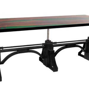 May include: A rectangular wooden table with a dark brown and green surface. The table is supported by a black metal base with adjustable height mechanisms. The table has a unique, industrial design.
