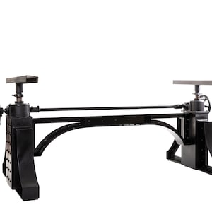 May include: Black metal table base with adjustable height. The base has a long, horizontal bar connecting two vertical supports. Each support has a wheel and a crank for adjusting the height.