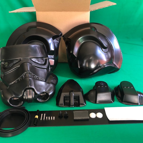 May include: A black plastic Star Wars Stormtrooper helmet kit with multiple pieces, including the helmet, back plates, and other accessories. The kit also includes a black rubber seal, screws, and a white sticker.