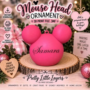 Może przedstawiać: Jasnoróżowa, kulista ozdoba z dwoma mniejszymi kulistymi uszami na górze, tworzącymi kształt głowy myszy. Imię Samara jest nadrukowane czarną kursywą z przodu. Ozdoba posiada małą pętelkę na górze, która służy do zawieszenia.