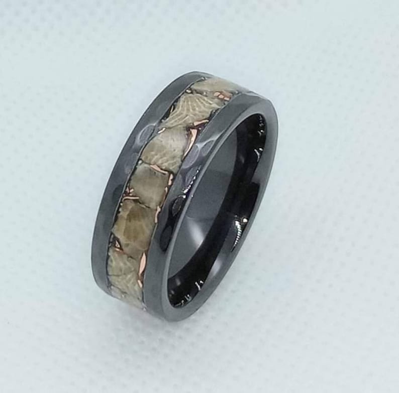 Pu&ograve; includere: Un anello in carburo di tungsteno nero con una fascia di intarsi in osso di dinosauro fossilizzato. L'anello ha una finitura lucida.