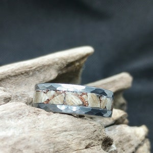 Pu&ograve; includere: Un anello d'argento con una fascia di metallo martellato e una fila di pietre bianche e rame incastonate.
