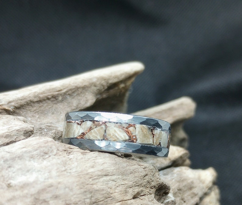 Pu&ograve; includere: Un anello d'argento con una fascia di metallo martellato e una fila di pietre bianche e rame incastonate.