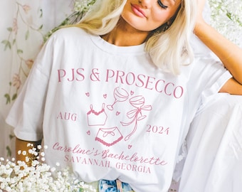 May include: White t-shirt with the text "PJS & PROSECCO" in pink, along with lingerie illustrations and the date "AUG 2024". The shirt also includes the text "Caroline's Bachelorette SAVANNAH, GEORGIA".