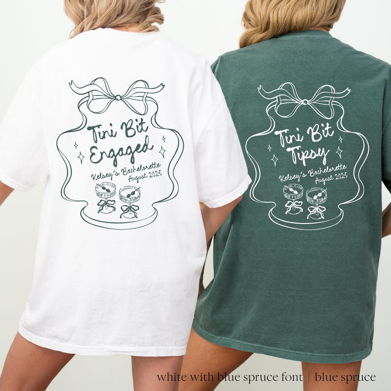 May include: Two white t-shirts with a green design. The design is a stylized illustration of a champagne flute with a bow on top. The text on the shirts reads "Tini Bit Engaged" and "Tini Bit Tipsy".