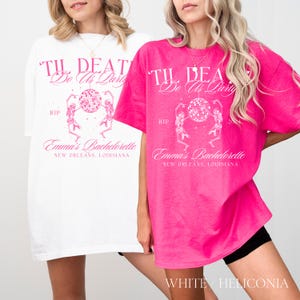 K&ouml;nnte beinhalten: Zwei &uuml;bergro&szlig;e T-Shirts, eines wei&szlig; und eines leuchtend rosa, zeigen den Text "Til Death Do Us Party" und "Emma's Bachelorette, New Orleans, Louisiana." Das Design umfasst eine Discokugel und tanzende Skelette. Die untere rechte Ecke des rosa Shirts lautet "WHITE / HELICONIA."