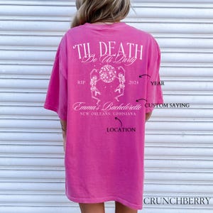 May include: Pink t-shirt with a white graphic design that says "Til Death Do Us Party" with skeletons dancing around a disco ball. The text also includes "Emma's Bachelorette", "New Orleans, Louisiana", "2024", and "Custom Saying".