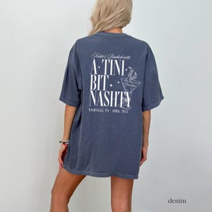 May include: A dark blue t-shirt with a white graphic that says "Katie's Bachelorette A TINI BIT NASTY Nashville, TN | April 2023".