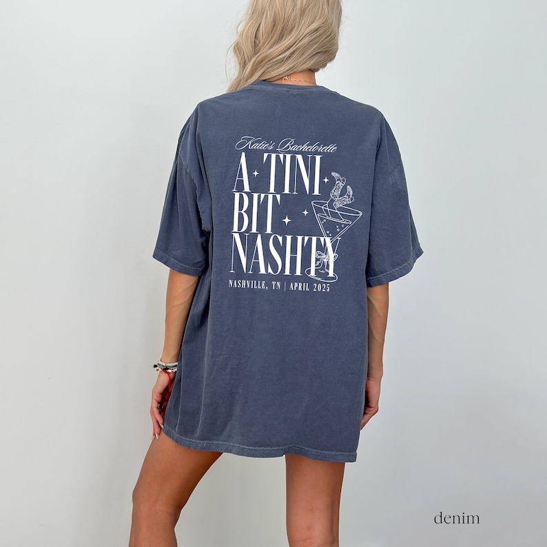 May include: A dark blue t-shirt with a white graphic that says "Katie's Bachelorette A TINI BIT NASTY Nashville, TN | April 2023".