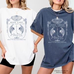 Op de afbeelding: Twee oversized T-shirts, &eacute;&eacute;n wit en &eacute;&eacute;n denimblauw, met een gedetailleerde afbeelding. De afbeelding bevat de tekst "HIGH LADY OF THE NIGHT COURT" en "INNER CIRCLE OF THE NIGHT COURT", een zwaard, vleugels en een bergontwerp. De tekst "MACY'S BACHELORETTE" is ook aanwezig.