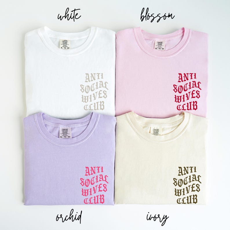 Puede incluir: Cuatro camisetas de diferentes colores con el texto "ANTI SOCIAL WIVES CLUB" en una fuente g&oacute;tica. Los colores son blanco, rosa, morado claro y crema.