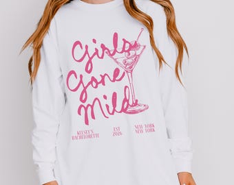 May include: White long-sleeve shirt with the text "Girls Gone Mild" in pink script, along with a pink martini glass graphic. The shirt also includes "Kelsey's Bachelorette", "EST 2026", and "New York" text.