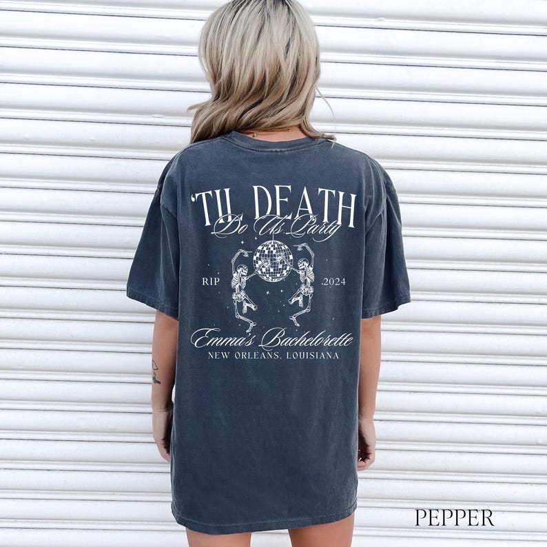 May include: A dark gray t-shirt with a white graphic print that says "Til Death Do Us Party" with two skeletons dancing around a disco ball. The text "RIP" and "2024" are on either side of the disco ball. Below the skeletons is the text "Emma's Bachelorette New Orleans, Louisiana."
