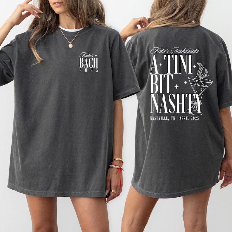 May include: Two gray t-shirts with white text. The front shirt says "Katie's Bach 2025". The back shirt says "Katie's Bachelorette A-TINI BIT NASHTY NASHVILLE, TN | APRIL 2025".