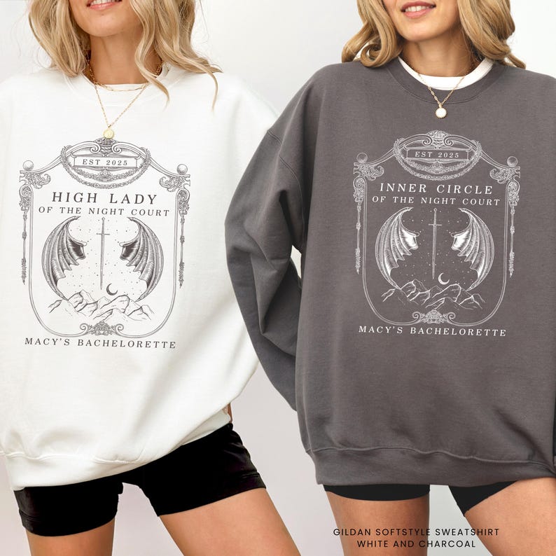 Op de afbeelding: Twee sweatshirts, &eacute;&eacute;n witte en &eacute;&eacute;n houtskoolkleurige, met een gedetailleerd grafisch ontwerp. Het witte sweatshirt toont "HIGH LADY OF THE NIGHT COURT" en de houtskoolkleurige leest "INNER CIRCLE OF THE NIGHT COURT". Beide bevatten "EST 2025" en "MACY'S BACHELORETTE".