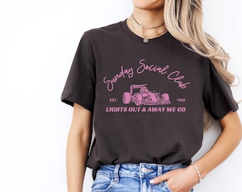 May include: A dark grey t-shirt with a pink graphic of a racing car and the text "Sunday Social Club Est. 1950 Lights Out & Away We Go".