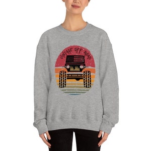 Puede incluir: Sudadera gris con un gr&aacute;fico de un jeep vintage todoterreno en un c&iacute;rculo con un fondo de puesta de sol. El texto "Vintage Off Road" est&aacute; escrito alrededor del c&iacute;rculo.