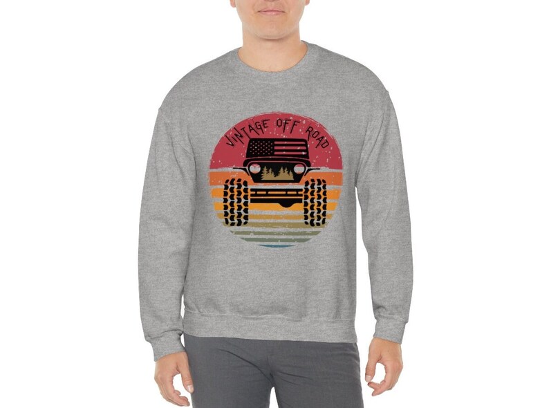 Puede incluir: Una sudadera gris con un gr&aacute;fico de un jeep vintage todoterreno. El gr&aacute;fico presenta una bandera estadounidense roja, blanca y azul, una puesta de sol y el texto "Vintage Off Road".