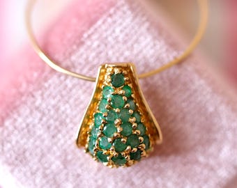 Könnte beinhalten: Eine goldene Anhänger-Halskette mit einem tropfenförmigen Design, gefüllt mit kleinen, runden Smaragdsteinen. Der Anhänger hängt an einer feinen Goldkette, vor einem weichen rosa Hintergrund.